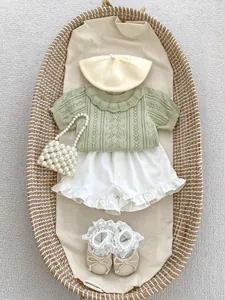 Flat lay of baby girl summer outfit with knit top, shorts, hat, bag and lace shoes
