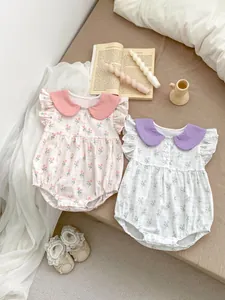 Barboteuses bébé à fleurs avec cols Claudine et manches volantées posées sur un lit