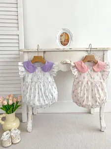 Détail de bodies fleuris pour bébés avec cols Peter Pan et manches à volants sur cintres