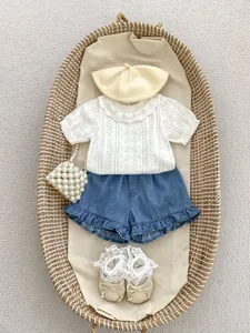 Flat lay of baby girl hollow knit top and denim shorts with lace socks and pearl bag