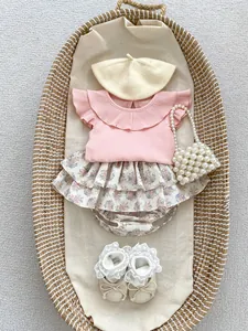 Flat lay of pink ruffled baby outfit with floral cake skirt pants and knit accessories