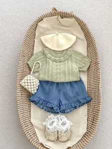 Flat lay of baby girl summer set with green knit top, denim shorts and accessories