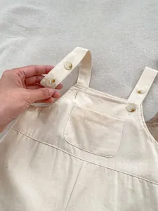 Detail of baby beige cotton romper featuring amber buttons and adjustable straps