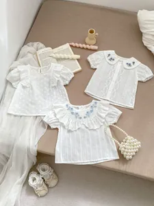 Detail der weißen Baumwollbluse für Mädchen mit blauer Blumenstickerei und Rüschenkragen