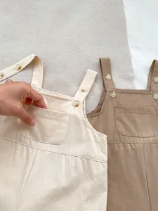 Detail shot of cotton baby overalls showing adjustable buttons and chest pockets in khaki