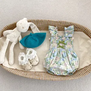 Détail d'un body floral pour bébé avec volants et nœuds en velours vert dans un panier