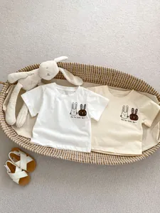 Dettaglio di magliette per neonati bianche e beige con stampe di conigli in un cesto
