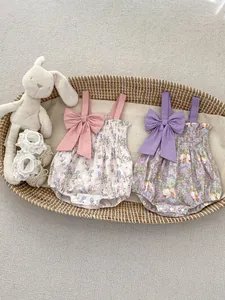 Detailed flat lay of floral baby rompers with large shoulder bows in a woven basket