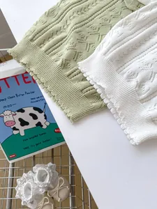 Close-up of hollow knit patterns and wavy edges on baby girl vest in mint and cream