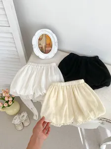 Flat lay of baby girl bubble shorts in white, apricot and black on a rustic wooden table