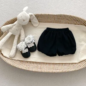 Flat lay of baby girl black bloomers and lace-trimmed shoes in a woven basket