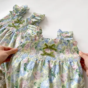 Détail de robe fleurie bébé avec smocks élastiques et nœuds en velours vert sur le buste