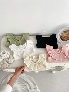 Flat lay of baby knit vests with ruffled collars and crisscross back straps in various colors