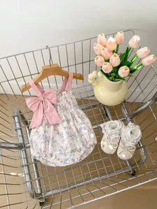 Close-up of baby floral romper with bow straps and lace shoes in a mini metal cart