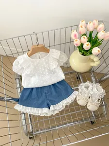 Flachbild von weißem Spitzenoberteil, Jeans-Shorts und Babyschuhen im Einkaufswagen