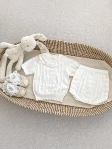 Flat lay of baby hollow knit short sleeve set with ruffle collar in a woven basket