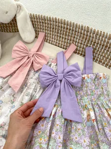 Close-up of floral baby bodysuits with oversized shoulder bows in a woven basket