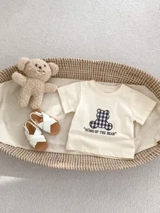 Dettaglio dell'outfit estivo bebè con t-shirt orsetto a quadri e sandali bianchi