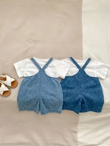 Flat lay of baby summer outfits featuring bear print denim overalls and white T-shirts