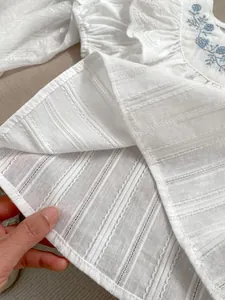 Detail der weißen Baumwollbluse für Mädchen mit blauer Blumenstickerei und Spitzen Rüschen