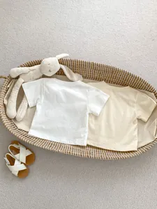 Vista dall'alto di due t-shirt in cotone per neonati in bianco e beige in un cesto