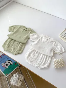 Flat lay of knit baby summer sets in sage green and cream with hollow lace details