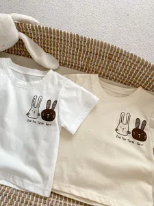 Dettaglio di magliette neonato in cotone bianco e beige con stampa coniglietto in un cesto