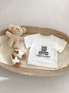 Close-up of white cotton baby t-shirt with bear patch and matching infant summer sandals