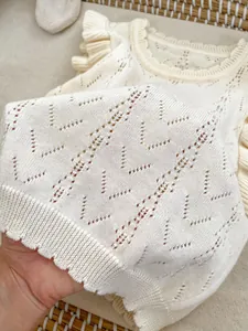 Detalle del tejido de punto calado crema y mangas con volantes en el chaleco de bebé