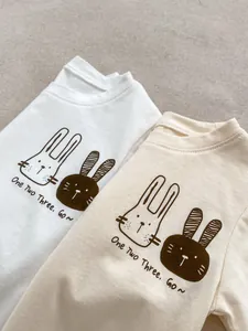 Dettaglio di t-shirt in cotone per neonati con graziose stampe di conigli in bianco e albicocca