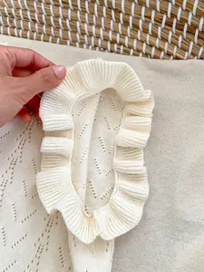 Vista detallada de top de punto color crema para niña con cuello de volantes y diseño calado