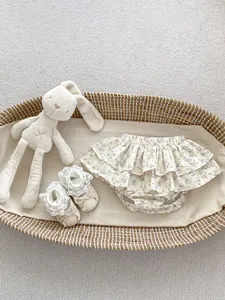 Floral baby bloomers with ruffles and lace soft-sole shoes in a cozy basket setup