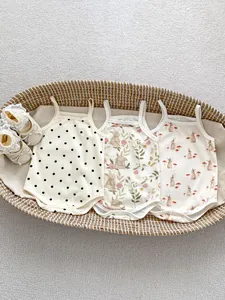 Flat lay of cotton baby bodysuits with rabbit prints and infant shoes in a basket