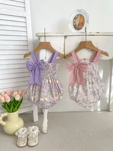 Detail of floral baby rompers with large shoulder bows and smocked chest on wooden hangers