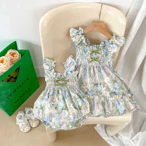 Détail d'un ensemble barboteuse florale et robe de sœur avec nœuds verts et volants
