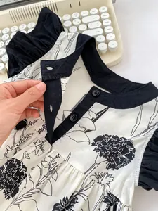 Detail of floral baby dress featuring black flower prints and ruffle neck with buttons
