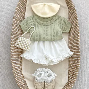 Sage green knitted baby set with hollow patterns and white shorts in a woven cradle