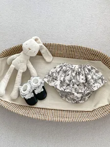 Detailed view of floral ruffle baby bloomers and lace bow shoes on a textured rug