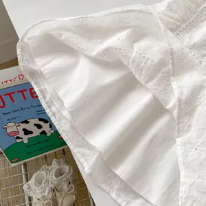 Close-up of white baby bodysuit with eyelet embroidery and delicate lace trim details