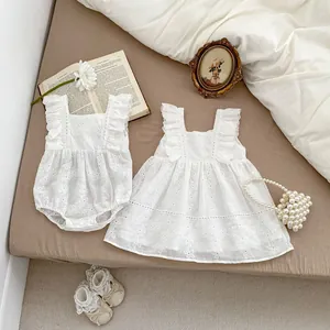 Detail of white cotton baby romper with floral hollow embroidery and ruffled straps