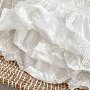 Close-up of white baby bodysuit featuring intricate hollow floral lace and crotch snaps