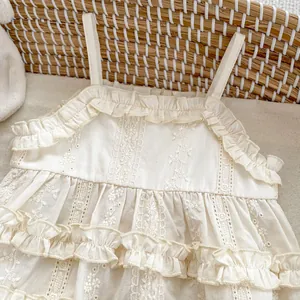 Detail of cream baby bodysuit featuring intricate floral lace embroidery and ruffles