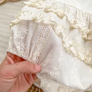 Close-up of floral embroidery and lace ruffles on cream cotton baby girl romper
