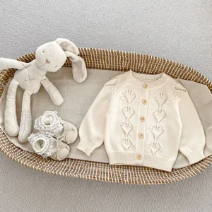 Detail of baby cream knit cardigan with hollow diamond pattern and soft lace shoes