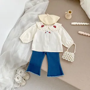 Dettaglio completo bambina: camicia beige con ricamo a fungo e jeans a zampa blu