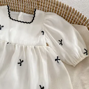 Detail of white infant tulle dress with black bow embroidery and wavy edge neckline