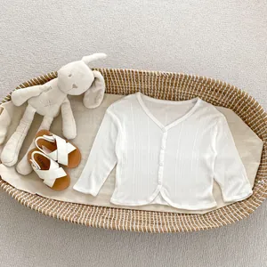 Dettaglio del cardigan in maglia bianca per neonati con scollo a V e bottoni nella culla