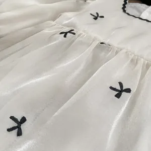 Detail of baby dress showing white satin fabric with black embroidery and pleated waist