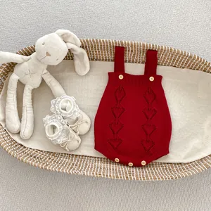 Detail of red knit baby romper with hollow heart patterns and yellow buttons