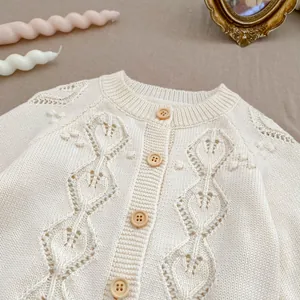 Detailed knit texture of a cream pointelle baby cardigan with brown wooden buttons